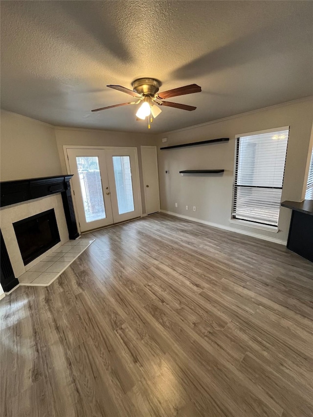 unfurnished living room with a ceiling fan, a textured ceiling, wood finished floors, french doors, and a fireplace