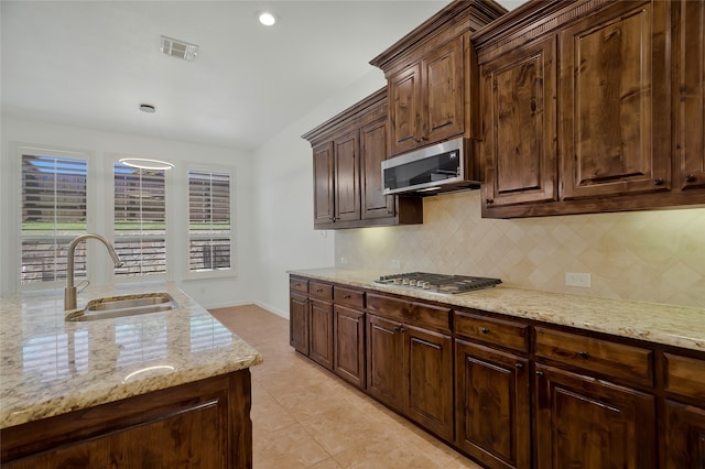 kitchen with backsplash, appliances with stainless steel finishes, dark brown cabinets, light stone countertops, and sink