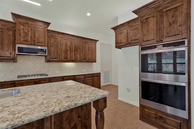 kitchen featuring stainless steel appliances, light tile patterned floors, backsplash, and light stone counters