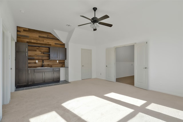 unfurnished living room featuring lofted ceiling, wooden walls, sink, light carpet, and ceiling fan