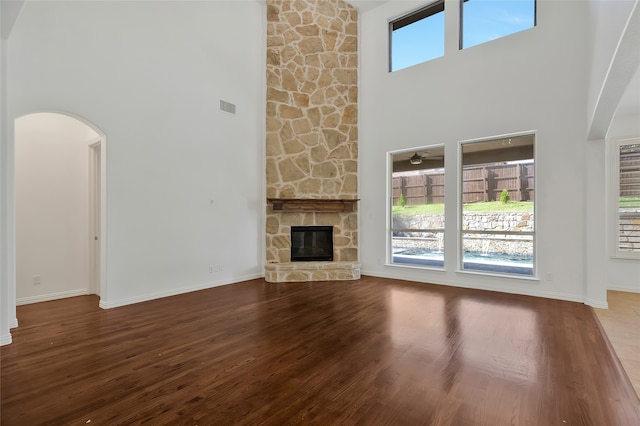 unfurnished living room with a wealth of natural light, wood-type flooring, a towering ceiling, and a stone fireplace