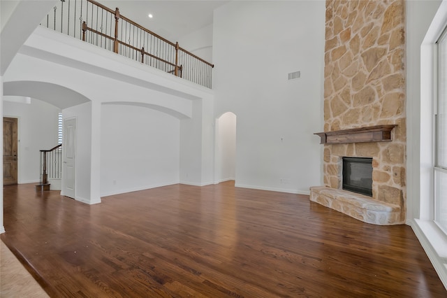 unfurnished living room with a towering ceiling, a stone fireplace, and dark hardwood / wood-style flooring