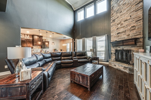 living room featuring dark wood-type flooring, a towering ceiling, and a stone fireplace