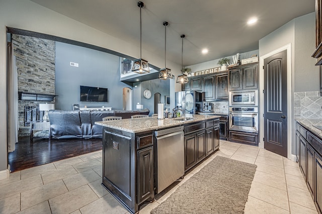 kitchen featuring stainless steel appliances, light wood-type flooring, decorative light fixtures, dark brown cabinetry, and an island with sink