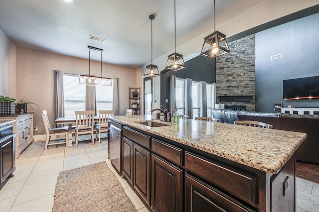 kitchen featuring hanging light fixtures, sink, an island with sink, and a fireplace