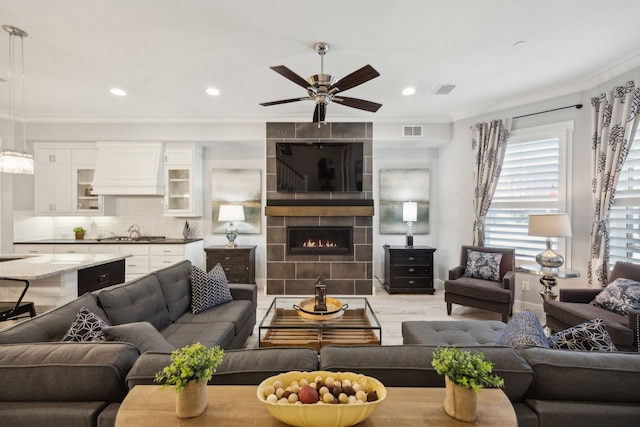 living room featuring ornamental molding, a large fireplace, sink, and ceiling fan