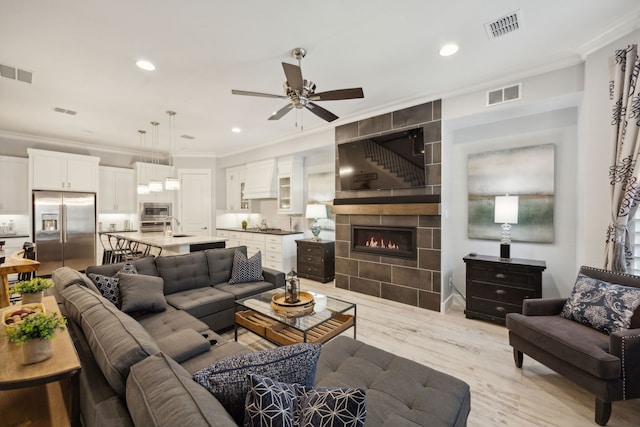 living room with light hardwood / wood-style floors, ceiling fan, a tile fireplace, and crown molding