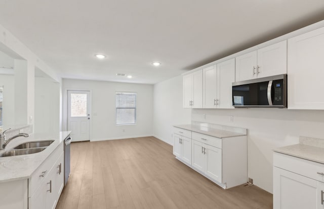 kitchen with white cabinetry, light stone countertops, sink, and light hardwood / wood-style flooring