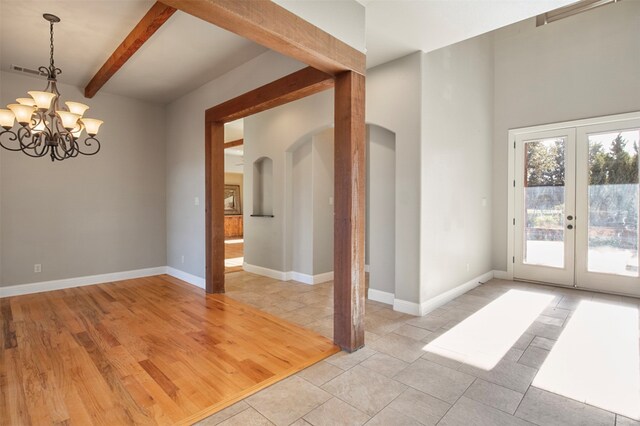 empty room featuring light wood-type flooring, a chandelier, french doors, and beamed ceiling