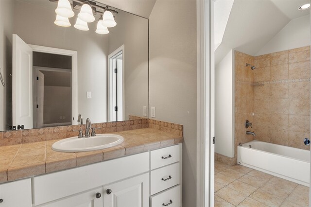 bathroom featuring vanity, tiled shower / bath, vaulted ceiling, and tile patterned flooring