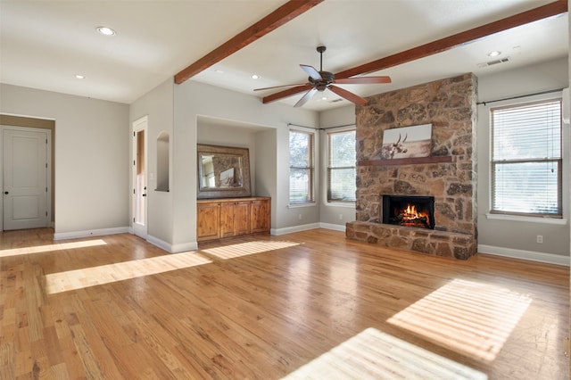 unfurnished living room featuring light wood-type flooring, a fireplace, a healthy amount of sunlight, and beam ceiling