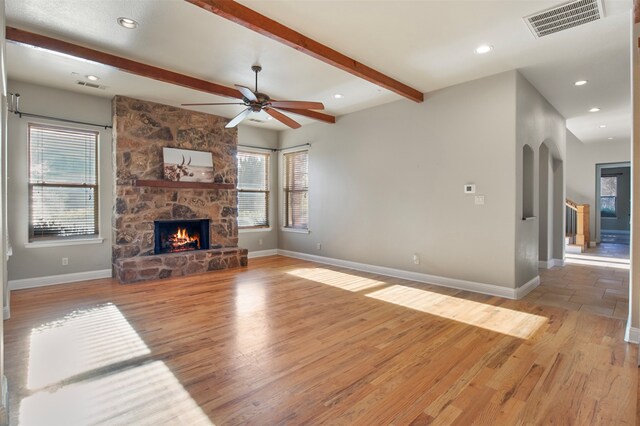 unfurnished living room with a fireplace, beamed ceiling, ceiling fan, and light hardwood / wood-style flooring