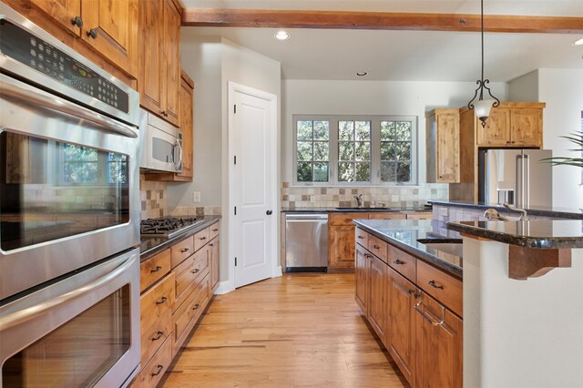 kitchen featuring stainless steel appliances, decorative light fixtures, a kitchen island with sink, light hardwood / wood-style flooring, and decorative backsplash