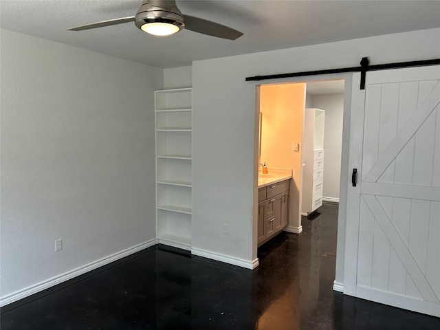 interior space with a textured ceiling, a barn door, ceiling fan, and ensuite bath