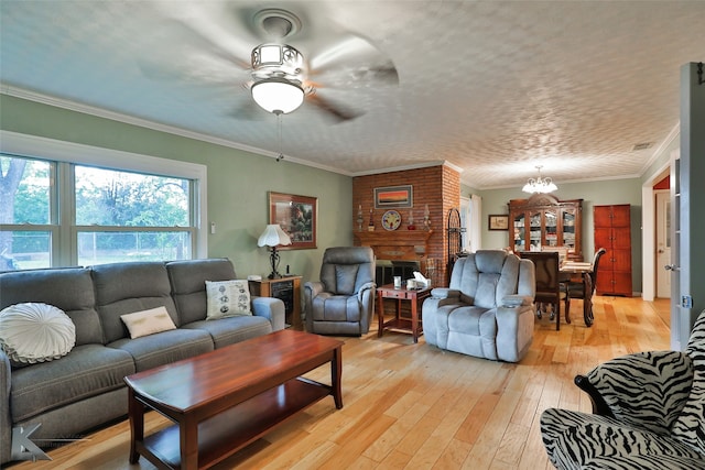 living room with light wood-type flooring, ceiling fan with notable chandelier, a fireplace, and crown molding