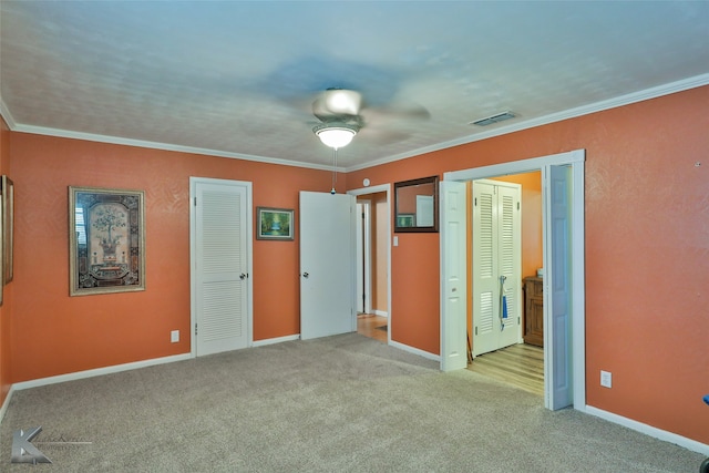 unfurnished bedroom with ornamental molding, light colored carpet, two closets, and ceiling fan