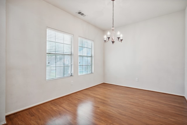 spare room featuring hardwood / wood-style flooring and a chandelier