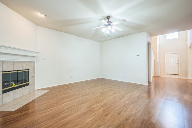 unfurnished living room featuring ceiling fan, a tiled fireplace, and light wood-type flooring