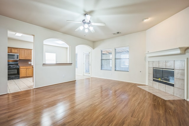 unfurnished living room with light wood-type flooring, plenty of natural light, ceiling fan, and a tile fireplace