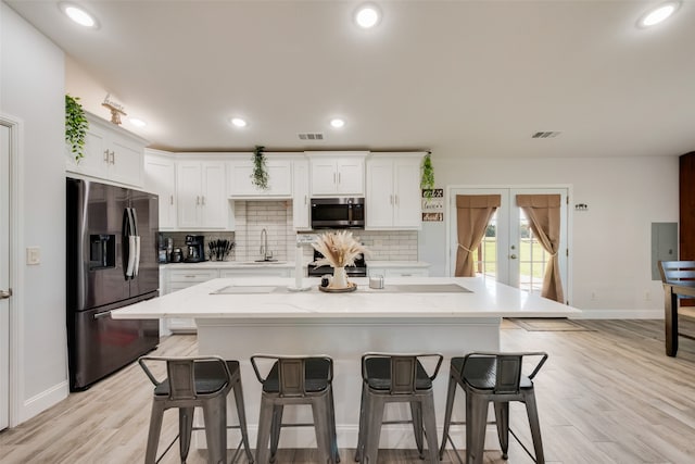 kitchen with white cabinetry, french doors, light hardwood / wood-style flooring, an island with sink, and appliances with stainless steel finishes