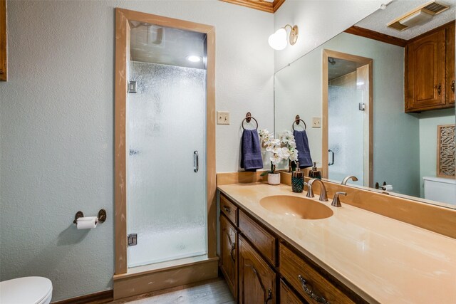 bathroom featuring wood-type flooring, toilet, vanity, crown molding, and a shower with shower door