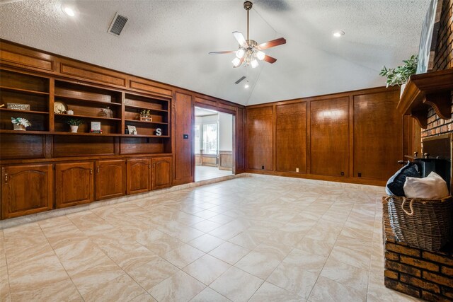 unfurnished living room featuring wood walls, built in shelves, ceiling fan, a textured ceiling, and high vaulted ceiling