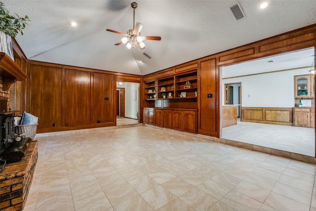 unfurnished living room with lofted ceiling, built in shelves, a textured ceiling, wooden walls, and ceiling fan