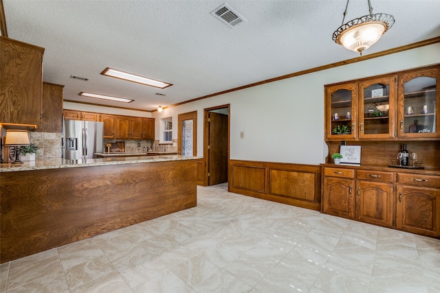 kitchen featuring hanging light fixtures, stainless steel refrigerator with ice dispenser, ornamental molding, light stone countertops, and a textured ceiling