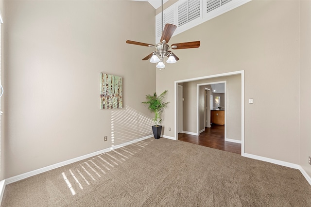 empty room with ceiling fan, dark carpet, and a high ceiling