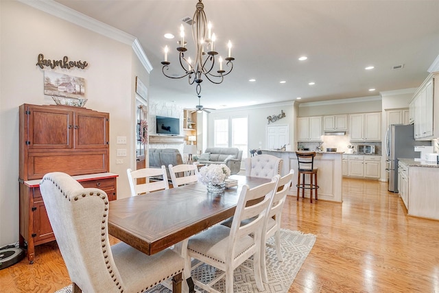 dining room with a fireplace, light hardwood / wood-style flooring, ceiling fan with notable chandelier, and ornamental molding