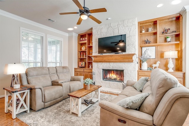 living room featuring crown molding, a fireplace, ceiling fan, and light wood-type flooring