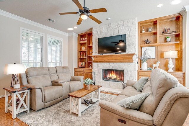 living room featuring light wood-style floors, visible vents, crown molding, and a stone fireplace