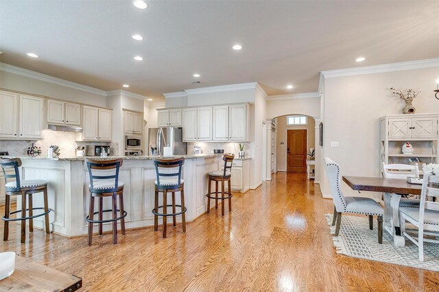 kitchen with appliances with stainless steel finishes, arched walkways, light stone counters, and a breakfast bar area