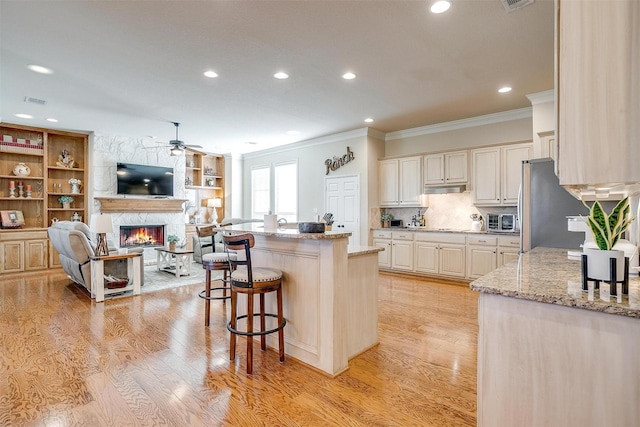 kitchen with stainless steel fridge, a fireplace, a kitchen island, light stone counters, and a breakfast bar area