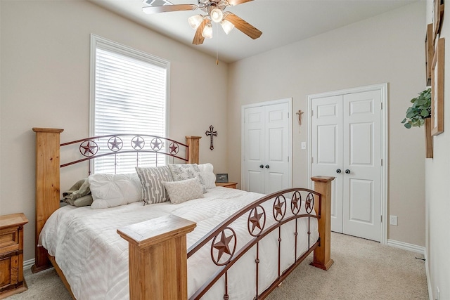 bedroom featuring baseboards, two closets, a ceiling fan, and light colored carpet