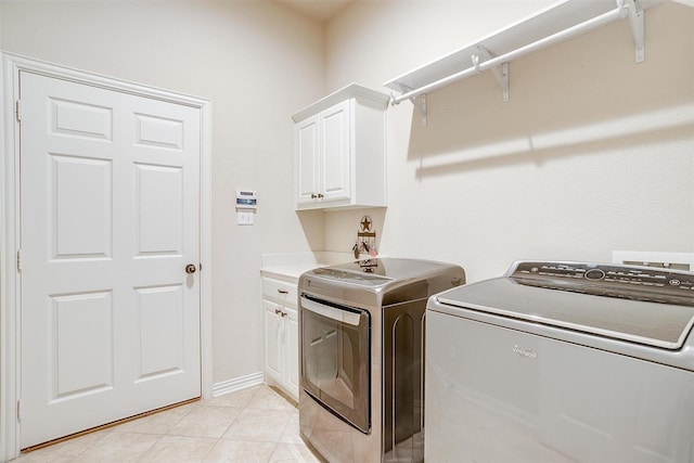 clothes washing area featuring separate washer and dryer, light tile patterned flooring, cabinet space, and baseboards