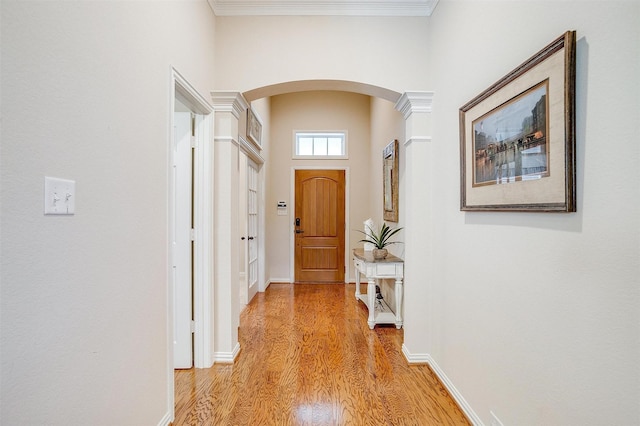 hallway with arched walkways, ornamental molding, light wood-style flooring, and baseboards