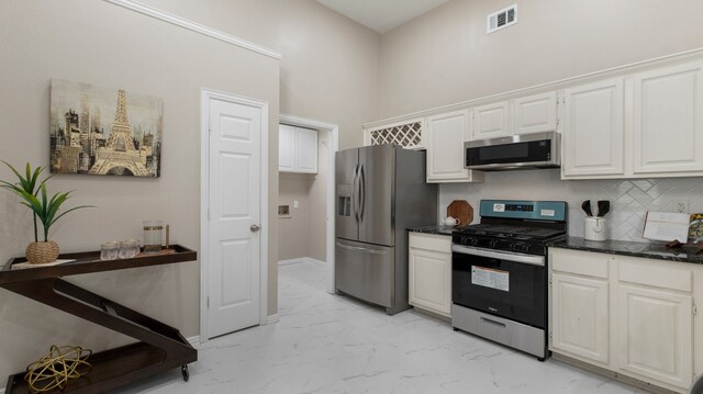 kitchen with a towering ceiling, stainless steel appliances, white cabinetry, and tasteful backsplash