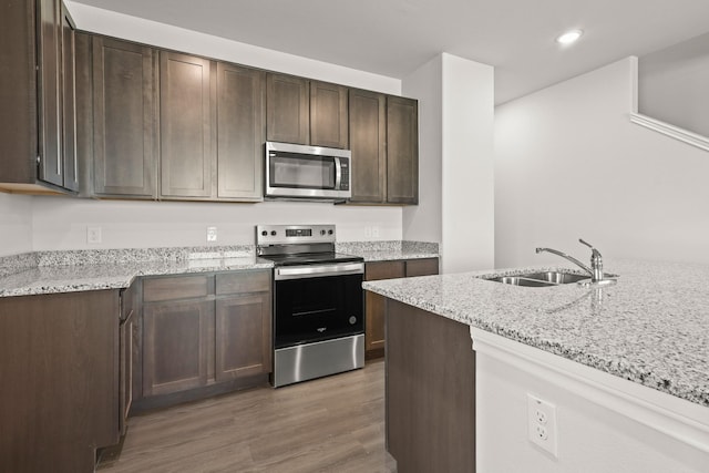 kitchen with appliances with stainless steel finishes, light stone counters, dark brown cabinetry, sink, and dark hardwood / wood-style floors