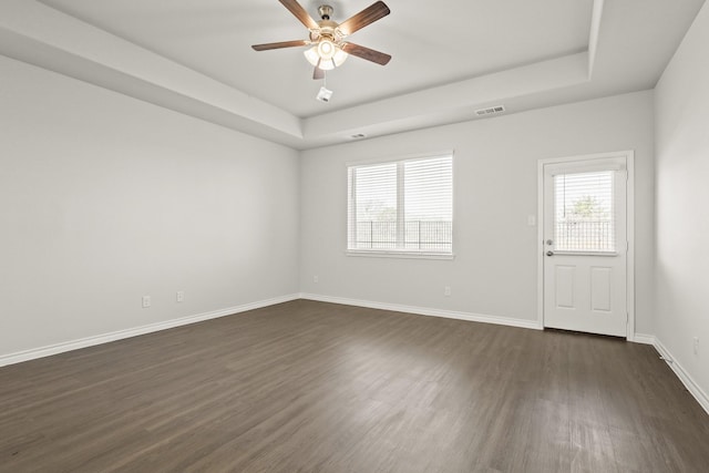 empty room with ceiling fan, dark hardwood / wood-style flooring, and a tray ceiling