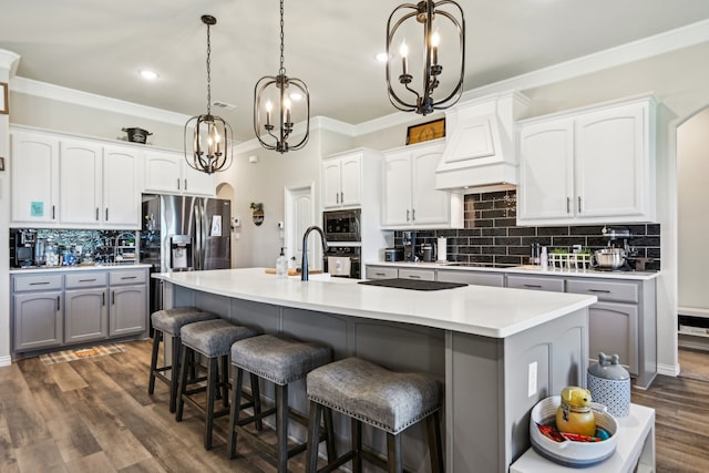 kitchen featuring decorative light fixtures, premium range hood, white cabinetry, and an island with sink