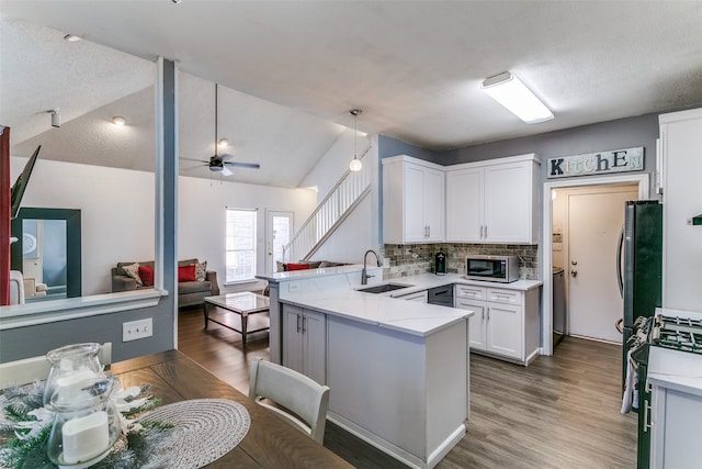 kitchen with vaulted ceiling, kitchen peninsula, a textured ceiling, white cabinetry, and appliances with stainless steel finishes