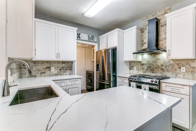 kitchen featuring wall chimney range hood, appliances with stainless steel finishes, sink, decorative backsplash, and white cabinets