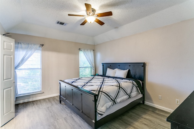 bedroom featuring hardwood / wood-style floors, lofted ceiling, multiple windows, and ceiling fan