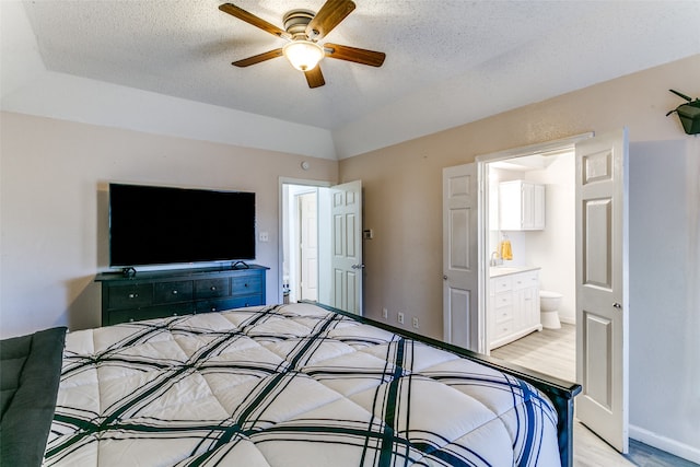 bedroom with ensuite bathroom, light wood-type flooring, a textured ceiling, and ceiling fan