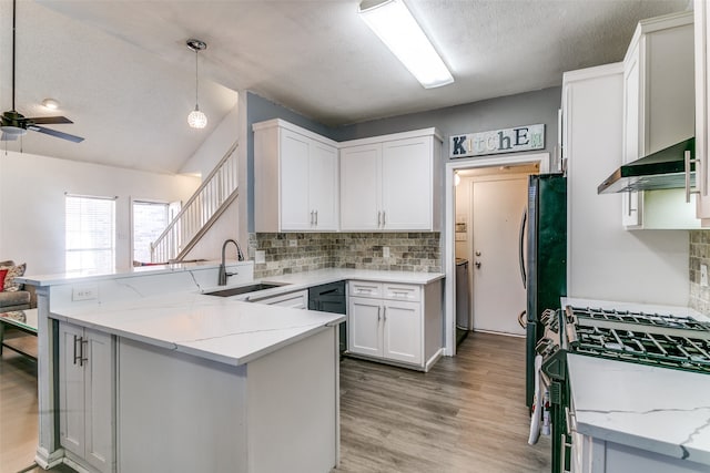 kitchen with white cabinets, kitchen peninsula, wall chimney exhaust hood, sink, and pendant lighting