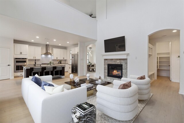 living room featuring a stone fireplace, a towering ceiling, and light hardwood / wood-style flooring