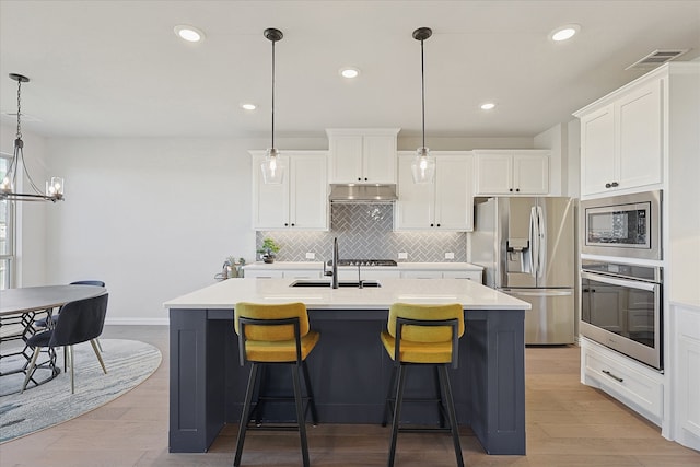 kitchen featuring a kitchen island with sink, hanging light fixtures, appliances with stainless steel finishes, and light hardwood / wood-style flooring