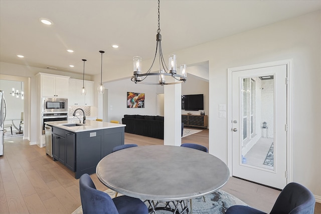 kitchen featuring white cabinets, a center island with sink, sink, hanging light fixtures, and appliances with stainless steel finishes