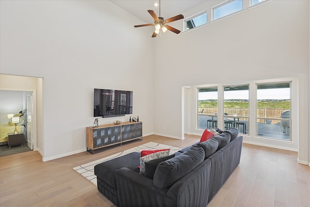 living room with ceiling fan, light wood-type flooring, and a towering ceiling